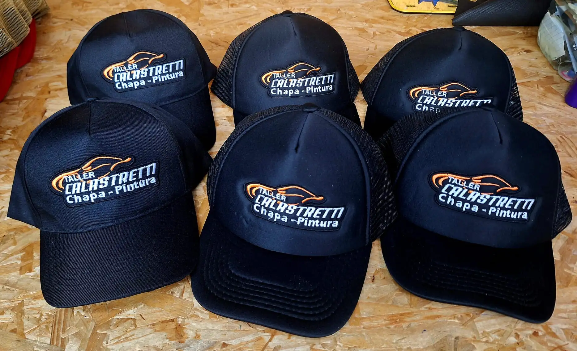 Gorras negras bordadas con el logo de Taller Calastretti Chapa y Pintura