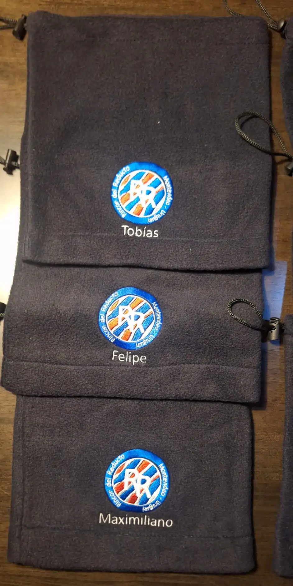Tres mochilas de vellón gris bordadas con el escudo de Rincón del Reducto y los nombres Tobías, Felipe y Maximiliano