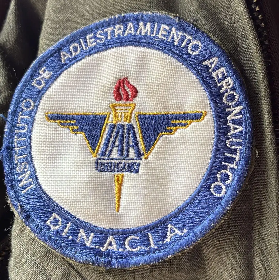Parche bordado circular del Instituto de Adiestramiento Aeronáutico B.I.N.A.C.I.A. sobre campera verde militar