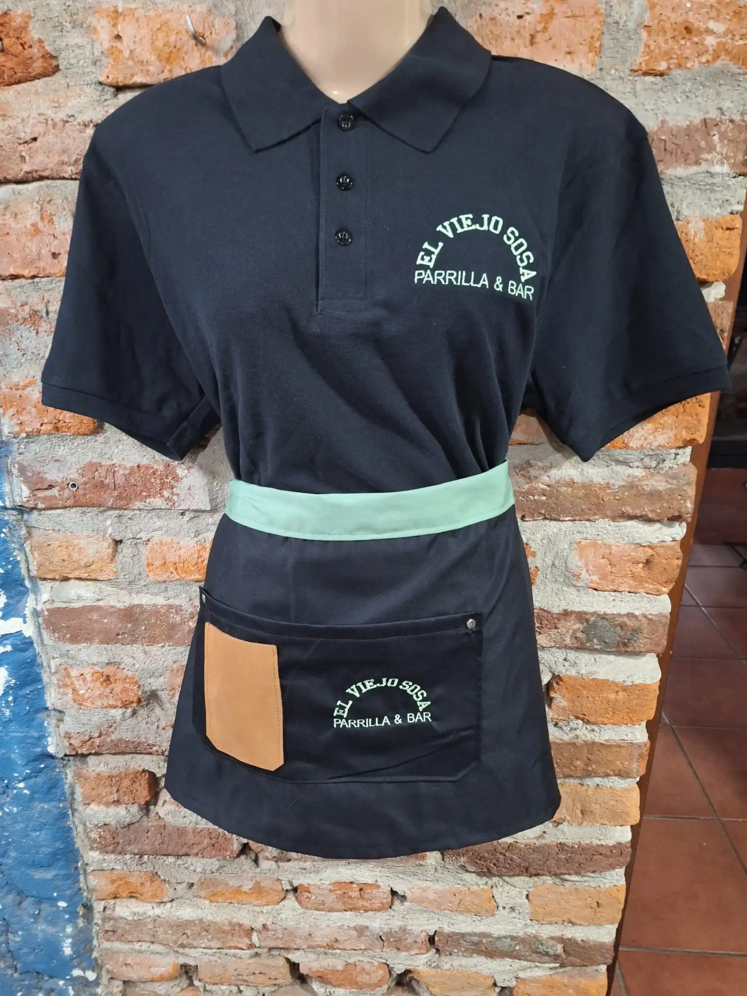 Uniforme de mozo de El Viejo Sosa Parrilla & Bar: polo azul y delantal con el logo bordado en verde claro